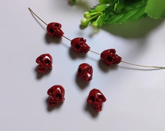 May include: Seven red skull-shaped beads, some strung on a thin gold wire. The beads are small and detailed, with a glossy finish.