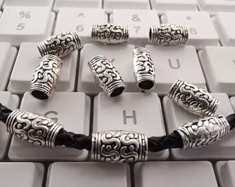 May include: Silver metal beads with a decorative pattern. The beads are on a black leather cord.