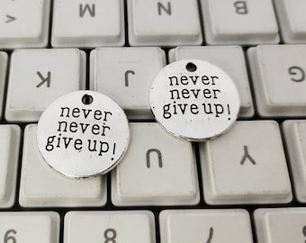 May include: Two silver charm pendants with the words "never never give up!" on a white keyboard.