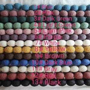 Pode incluir: Uma coleção de 13 contas de rocha vulcânica de diferentes cores. As contas estão dispostas em filas, cada fila representa uma cor diferente. As cores são: azul, rosa, verde escuro, verde claro, rosa claro, roxo, branco, amarelo, marrom, azul escuro, cinza, vermelho e preto.