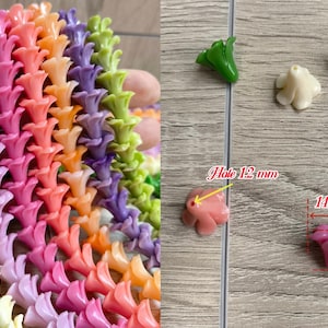 May include: A collection of multi-colored flower-shaped beads in green, cream, pink, orange, and purple. The beads measure 14 mm in width and 12 mm in height, with a 1.2 mm hole. The beads are arranged in vertical strands and as individual pieces.