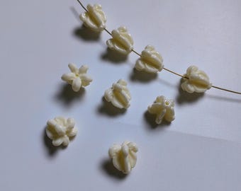 May include: Ivory-colored flower-shaped beads, some strung on a thin wire, others scattered. The beads have a detailed, textured surface, resembling small blossoms. Ideal for jewelry making or craft projects.