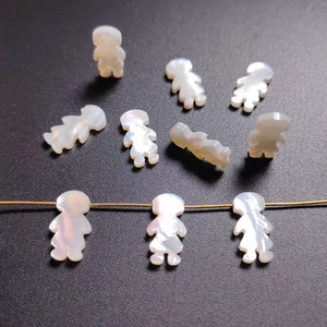 May include: A collection of white mother of pearl shell charms shaped like people. The charms are strung on a gold wire.