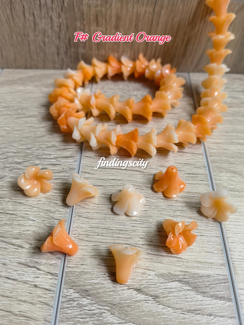 May include: A strand of gradient orange flower-shaped beads arranged in a coil, accompanied by several loose individual flower beads. The text F# Gradient Orange and findingscity are visible on the image. The beads feature a translucent finish.