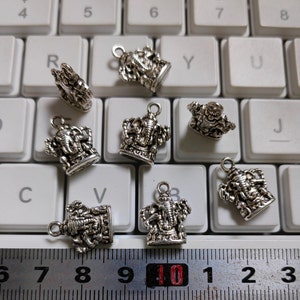 May include: A collection of silver-colored Ganesha charms, each with a loop for hanging. The charms are intricately detailed and displayed on a white keyboard. A ruler is at the bottom, showing measurements.