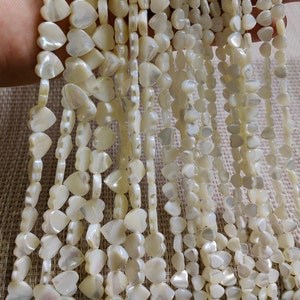 May include: A strand of white mother of pearl heart shaped beads. The beads are strung on a clear thread and are approximately 10mm in size.