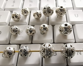 May include: A collection of silver metal beads with intricate designs. The beads are arranged on a white keyboard with black keys.