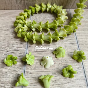 May include: A strand of gradient green flower-shaped beads and several loose individual beads. The beads feature a bell-like shape with five petals and a central hole for stringing. The text H# Gradient Green and findingscity are visible.