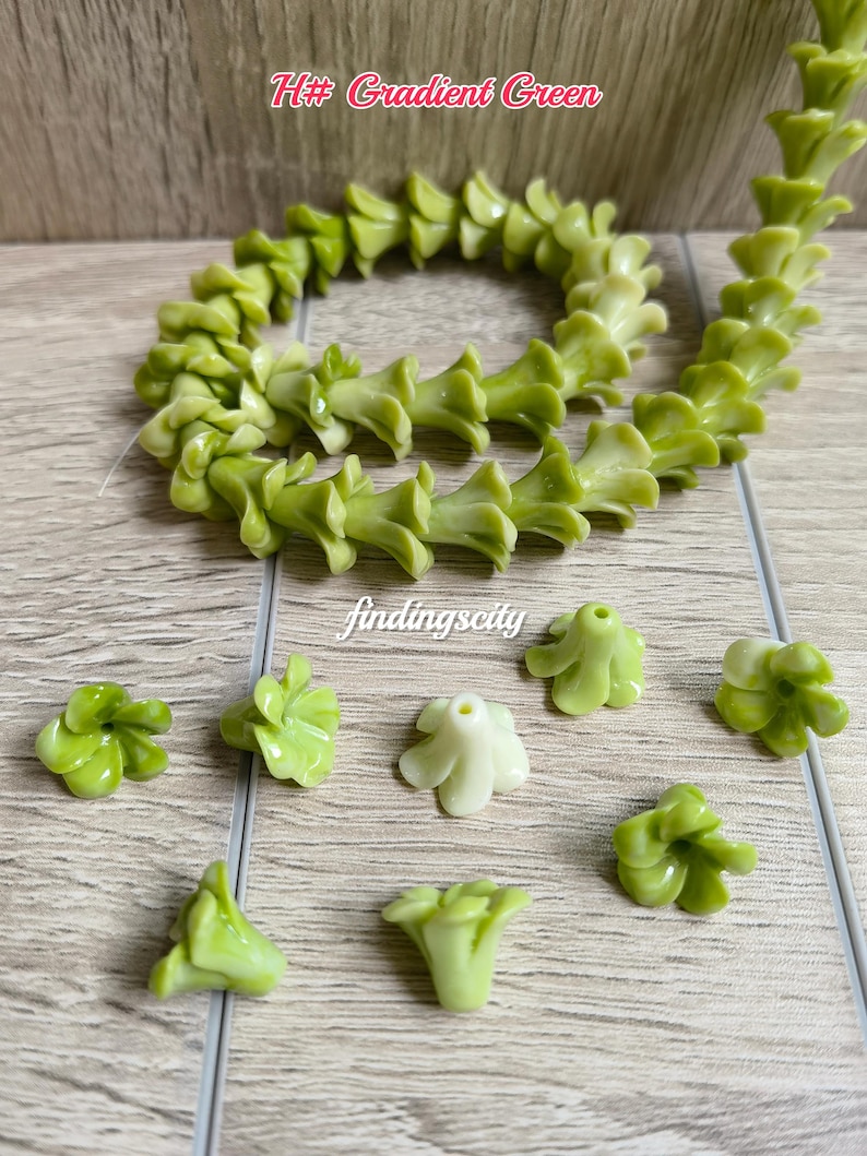 May include: A strand of gradient green flower-shaped beads and several loose individual beads. The beads feature a bell-like shape with five petals and a central hole for stringing. The text H# Gradient Green and findingscity are visible.