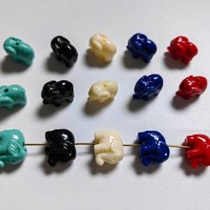 May include: A collection of colourful elephant-shaped beads in various colours, including turquoise, black, white, blue, and red. The beads are strung on a thin wire.