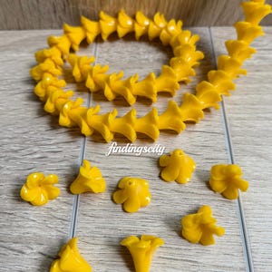 May include: A string of bright yellow flower-shaped beads arranged in a circular pattern, accompanied by several loose individual flower beads. The text K# Yellow and findingscity are visible in the image. The beads feature a five-petal design.