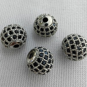 May include: Four silver round beads with a black diamond-like pattern. The beads have a hole in the centre for stringing.