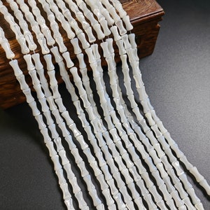 Puede incluir: Una hebra de cuentas de concha blanca con forma cilíndrica. Las cuentas están dispuestas en fila y tienen un acabado liso y pulido.