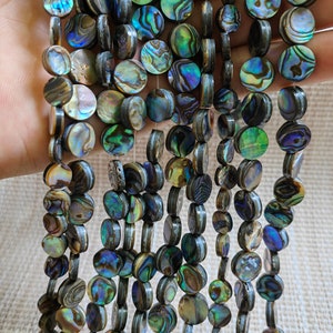 May include: A strand of iridescent abalone shell beads. The beads are round and flat, with a dark brown outer edge and a colorful, iridescent interior. The beads are strung on a clear thread.
