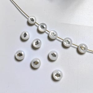 May include: A string of white round beads with a silver cloud design. The beads are strung on a gold wire.