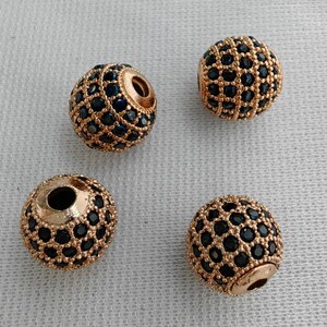 May include: Four gold-toned round beads with a black and gold geometric pattern. The beads are made of metal and have a shiny finish.