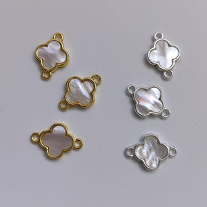 Puede incluir: Cinco abalorios en forma de trébol de oro y plata con inserciones de nácar blanco. Los abalorios tienen dos anillos de salto para sujetarlos a joyas.