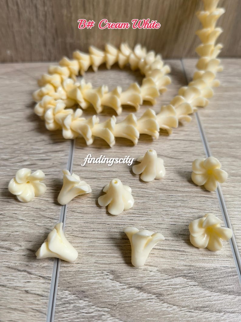 May include: A long string of cream white flower-shaped beads arranged in a coil, accompanied by several individual loose flower beads. Each bead features a central hole for threading. The text B# Cream White and findingscity is visible.