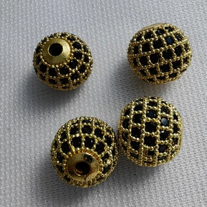 May include: Four gold-coloured round beads with a black grid pattern. The beads are approximately 2.5 cm in diameter.