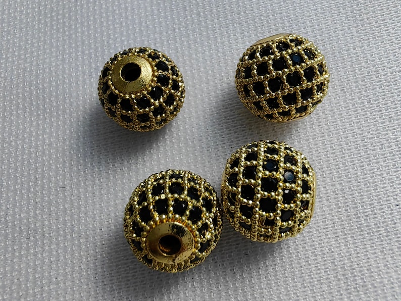 May include: Four gold-coloured round beads with a black grid pattern. The beads are approximately 2.5 cm in diameter.