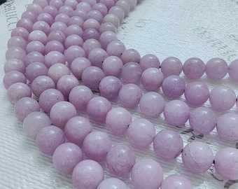 Puede incluir: Una hebra de cuentas de color lavanda pálido, dispuestas en semicírculo, mostrando la forma redonda y lisa y las sutiles variaciones de color de cada cuenta.