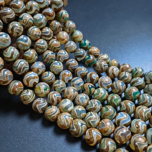 Può includere: Primo piano di più fili di perline rotonde. Le perline hanno un aspetto marmorizzato con vortici marroni, verdi e bianchi. Le perline sono infilate insieme, creando un display strutturato e colorato. Ideale per la creazione di gioielli.