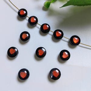May include: A strand of black beads with red heart accents. The beads are round and have a glossy finish.