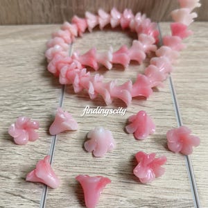 May include: A strand of gradient pink flower-shaped beads and several loose individual flower beads. The text 1# Gradient Pink and findingscity are visible. The beads feature a translucent, light pink to darker pink color transition.
