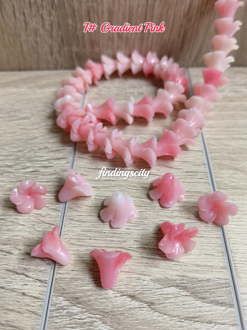 May include: A strand of gradient pink flower-shaped beads and several loose individual flower beads. The text 1# Gradient Pink and findingscity are visible. The beads feature a translucent, light pink to darker pink color transition.