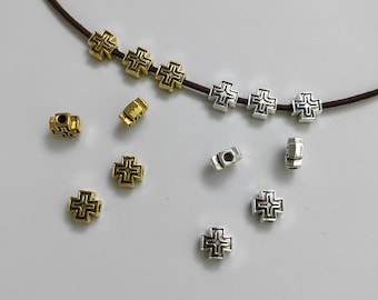 May include: A collection of silver and gold cross-shaped beads with intricate designs. The beads are strung on a brown cord.