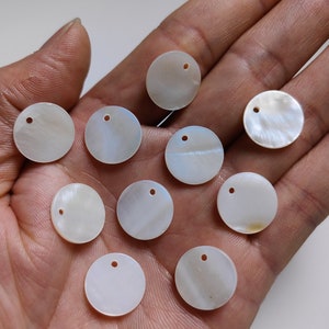 May include: Ten white, round, iridescent shell discs with a hole in the center. Each disc measures 15 mm in diameter. The discs are arranged in a semi-circle on a hand.