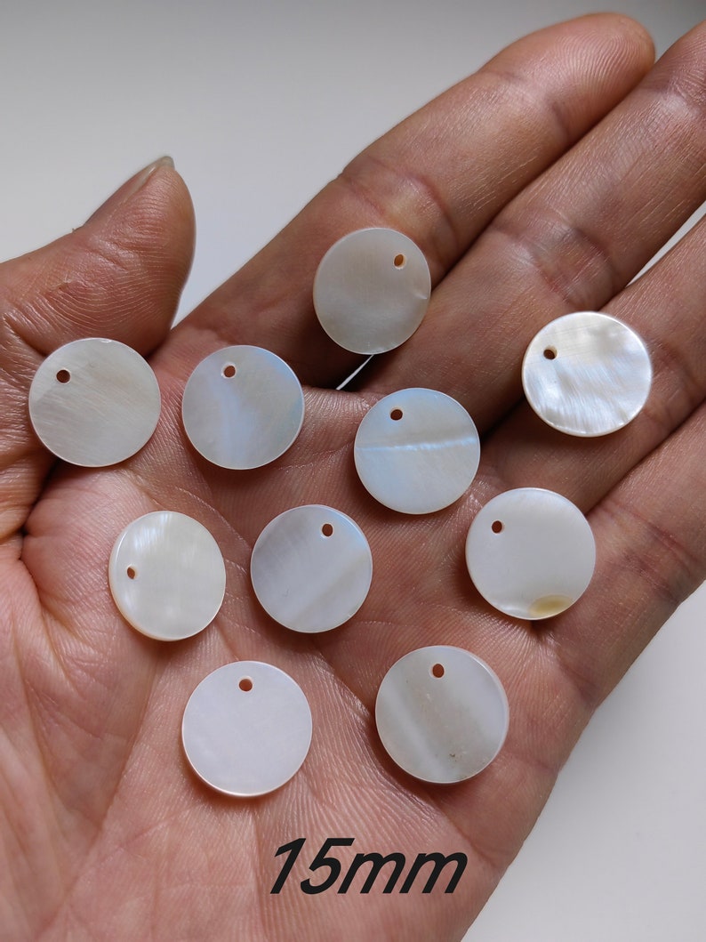 May include: Ten white, round, iridescent shell discs with a hole in the center. Each disc measures 15 mm in diameter. The discs are arranged in a semi-circle on a hand.
