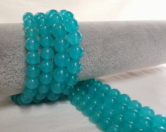 Peut inclure: Un brin de perles de pierres précieuses bleu turquoise. Les perles sont rondes et lisses, et elles sont enfilées sur un fil transparent. Les perles sont disposées en une spirale lâche.