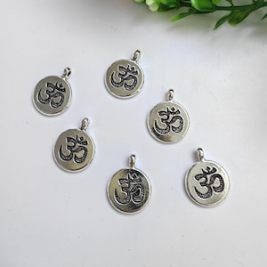 May include: Six silver-toned metal charms with an Om symbol in black. The charms are round and have a loop at the top for attaching to a necklace or bracelet.