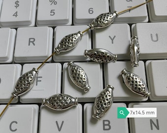 May include: Silver oval-shaped beads with a decorative pattern. The beads are approximately 7x14.5 millimeters in size and are strung on a gold wire.