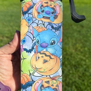 May include: A blue and white stainless steel water bottle with a black lid and a carrying handle. The bottle features a repeating pattern of Stitch from Lilo & Stitch carving pumpkins with bats and spiderwebs in the background.