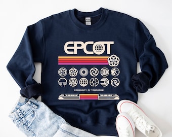 May include: A navy blue sweatshirt with a retro-style graphic of the Epcot logo and various park icons. The text "EPCOT" is in a cream color with a rainbow stripe behind it. The text "Community of Tomorrow" is printed below the icons.
