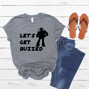 May include: Gray t-shirt with a black silhouette of Buzz Lightyear from Toy Story and the text "Let's Get Buzzed".