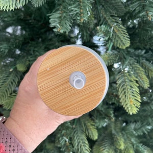May include: A close-up of a white tumbler with a bamboo lid. The lid has a small hole in the center for a straw.