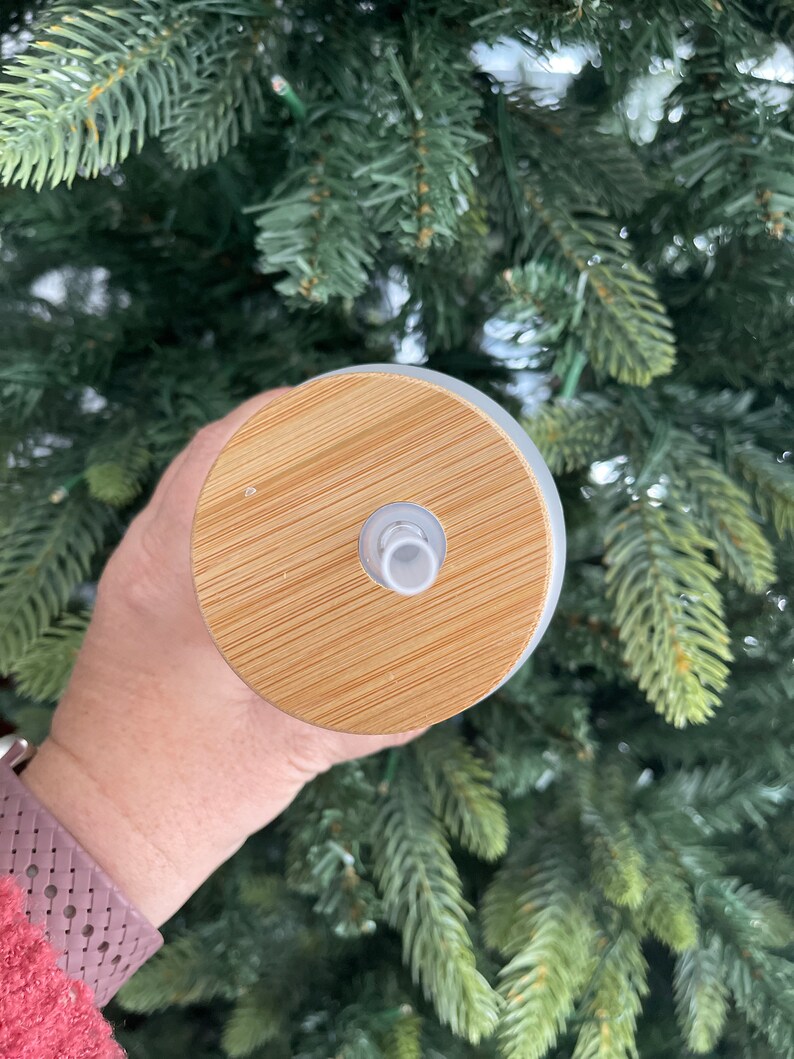 May include: A close-up of a white tumbler with a bamboo lid. The lid has a small hole in the center for a straw.