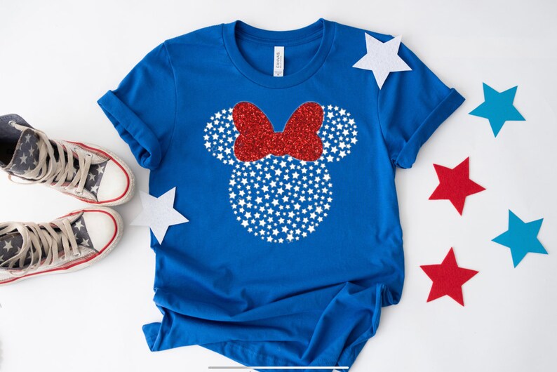 May include: A blue t-shirt with a white and red glitter Mickey Mouse head design. The design features white stars and a red bow.