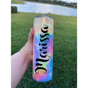 Puede incluir: Un vaso de acero inoxidable con un patr&oacute;n de tie-dye en tonos de rosa, amarillo, azul y verde. El vaso tiene una calcoman&iacute;a de vinilo negro con el nombre "Marissa" en &eacute;l.