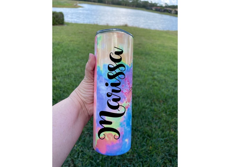 Puede incluir: Un vaso de acero inoxidable con un patr&oacute;n de tie-dye en tonos de rosa, amarillo, azul y verde. El vaso tiene una calcoman&iacute;a de vinilo negro con el nombre "Marissa" en &eacute;l.