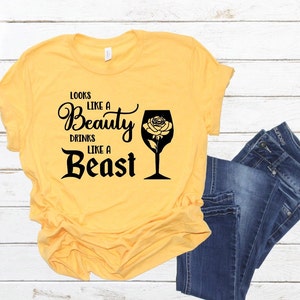 May include: Yellow t-shirt with black text that reads "Looks like a Beauty drinks like a Beast" and a black silhouette of a wine glass with a rose inside.