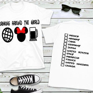 May include: Two white t-shirts, one with the text "Drinking Around the World" and a globe, Mickey Mouse ears with a red bow, and a beer mug, the other with a checklist of countries including Mexico, Norway, China, Germany, Japan, United States, Italy, Morocco, France, United Kingdom, and Canada.