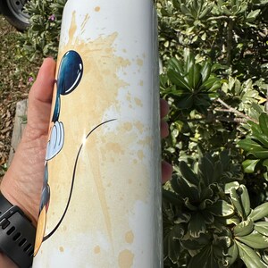 May include: White stainless steel water bottle with a black lid and a cartoon image of Mickey Mouse in a yellow and white watercolor design.