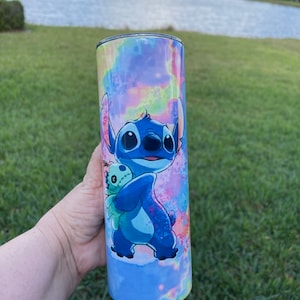 Puede incluir: Un vaso de acero inoxidable azul y morado con un dise&ntilde;o tie-dye y una imagen de dibujos animados de Stitch de Lilo & Stitch sosteniendo un juguete de peluche.