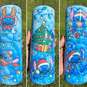 Może przedstawiać: Niebieski i biały kubek z motywem świątecznym z Stitch'em z Lilo & Stitch. Kubek ma niebieskie tło z białymi płatkami śniegu i świątecznymi światełkami. Stitch ma na sobie czapkę Mikołaja i trzyma laskę cukrową.
