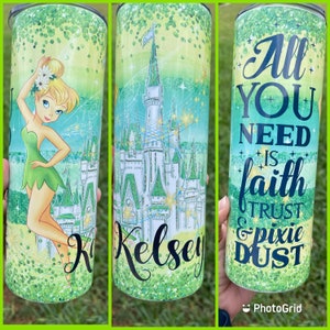 May include: A green and white tumbler with a glitter finish. The tumbler features a cartoon image of Tinkerbell in front of Cinderella's Castle. The text "All you need is faith & pixie dust" is printed on the tumbler.
