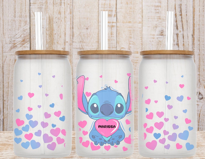 May include: Three white can-shaped tumblers with bamboo lids and clear straws. The center tumbler features a blue Stitch character holding a pink heart with the name "MARISSA" on it. All three tumblers have a background of pink and purple hearts.